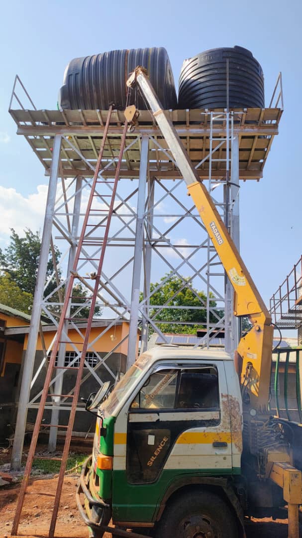 Crane lifting water tanks onto an elevated steel tower Uganda
